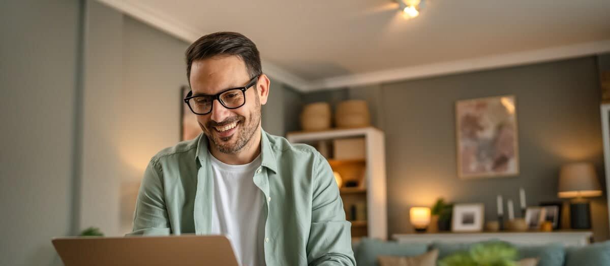 Homme souriant utilisant un ordinateur portable, illustrant le portage salarial et le travail flexible.